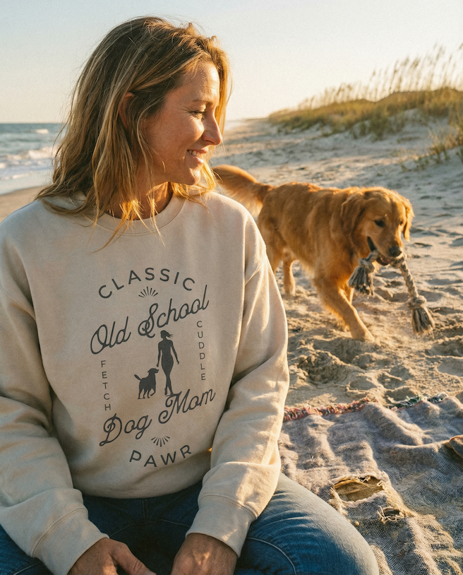 Woman wearing a 'Classic Old School Dog Mom' sweatshirt on a beach with a dog.