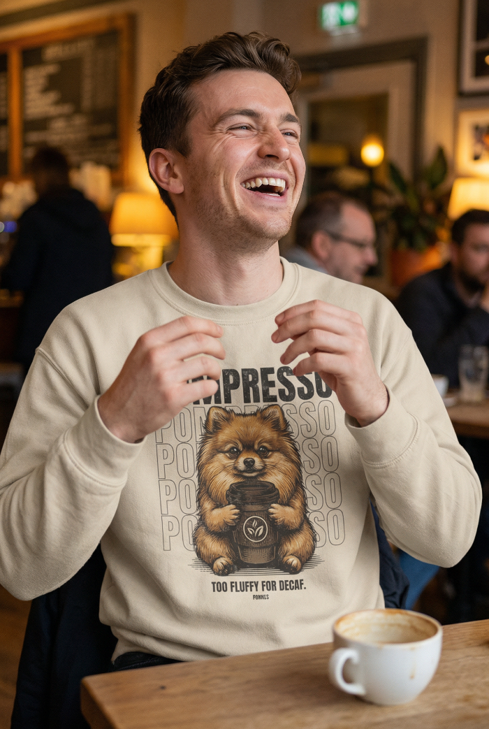 Man laughing in a café wearing a sweatshirt with a bear graphic and text.