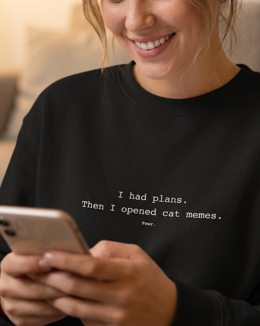Woman wearing a black sweatshirt with text, using a phone indoors.