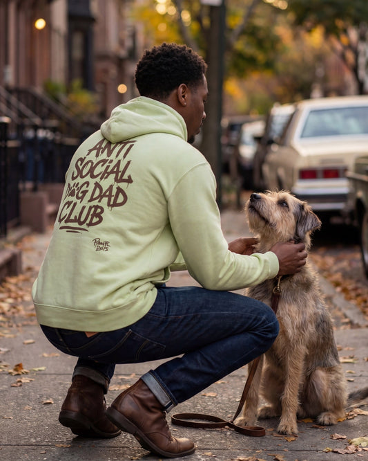 Man in a light green hoodie with text Anti Social Dog Dad Club on the back, petting a dog on a city street.