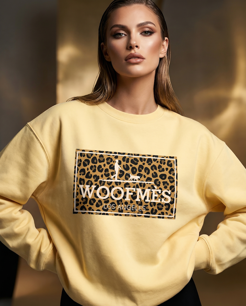 Woman wearing a yellow sweatshirt with a leopard print logo and text. Woofmes logo