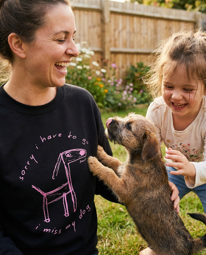 Woman wearing a black sweatshirt with a dog graphic and text, interacting with a child and a puppy in a garden.
