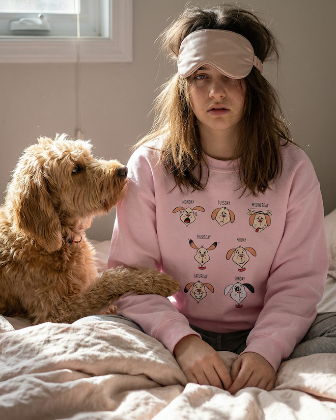 Girl in pink sweatshirt with dog on bed