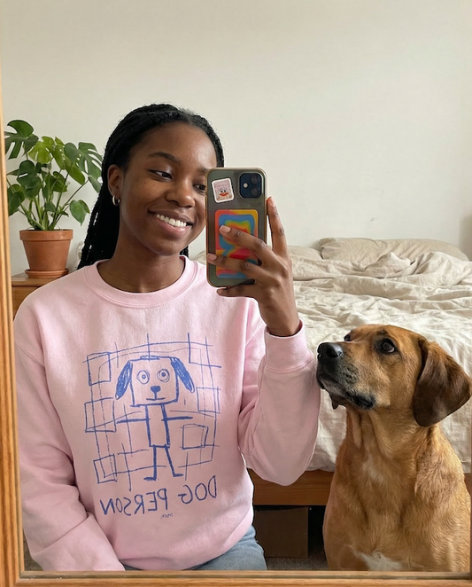 Woman taking a mirror selfie wearing a pink PAWR dog person sweatshirt with playful dog illustration, sitting next to her dog at home, perfect for dog moms, dog lovers, and cozy everyday wear.