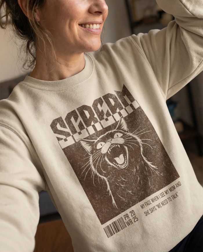 Person wearing a beige sweatshirt with a graphic design of a cat and text.