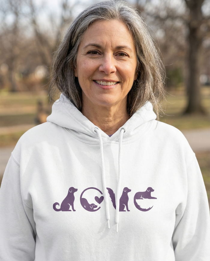 Woman smiling outdoors wearing a white PAWR dog love hoodie with minimalist purple dog graphic, cozy unisex fit, perfect for dog moms, dog dads, and everyday dog lover style.