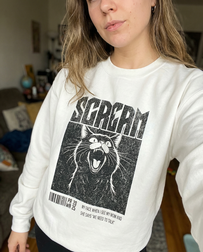 Person wearing a white sweatshirt with a graphic design of a cat and text.